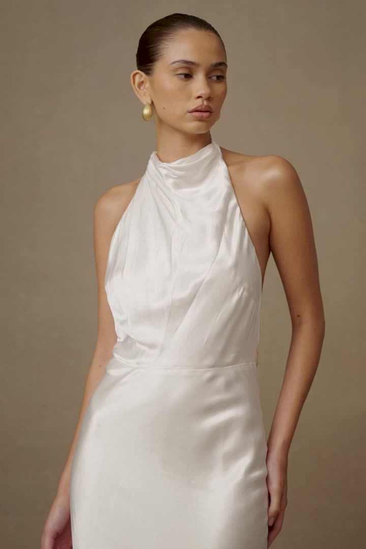 This may contain: a woman wearing a white dress with a halter neckline and gold hoop earrings