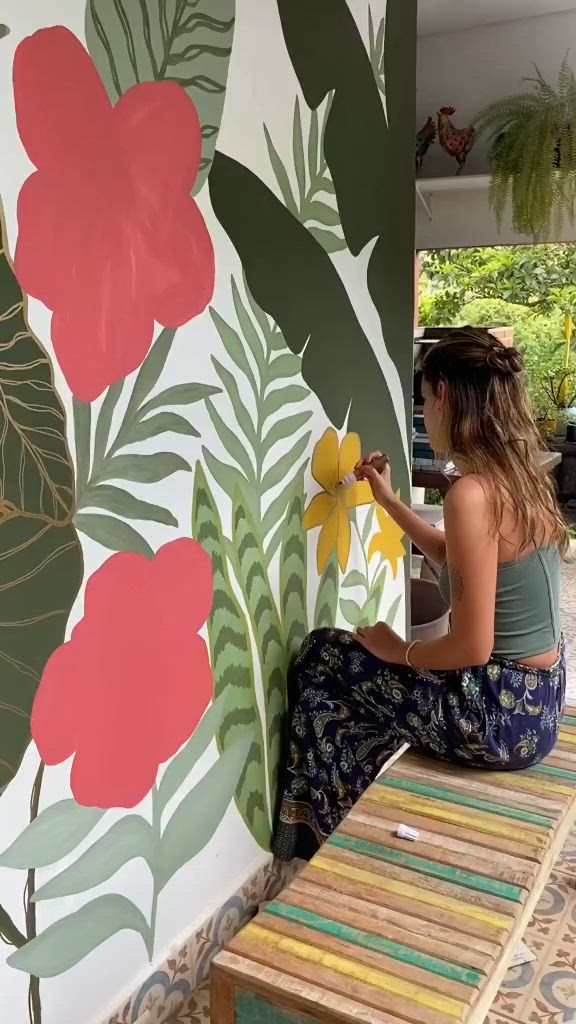 This may contain: a woman painting a wall with flowers and leaves