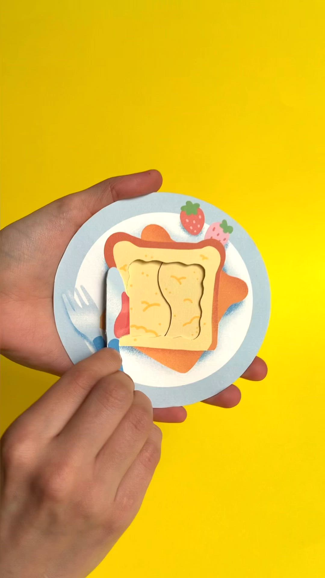 This may contain: a person holding a piece of paper cut out of toast on a plate with strawberries