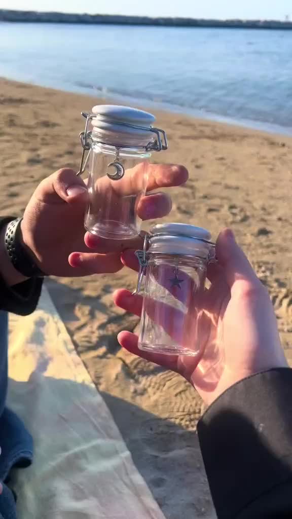 This may contain: two people are holding small jars on the beach