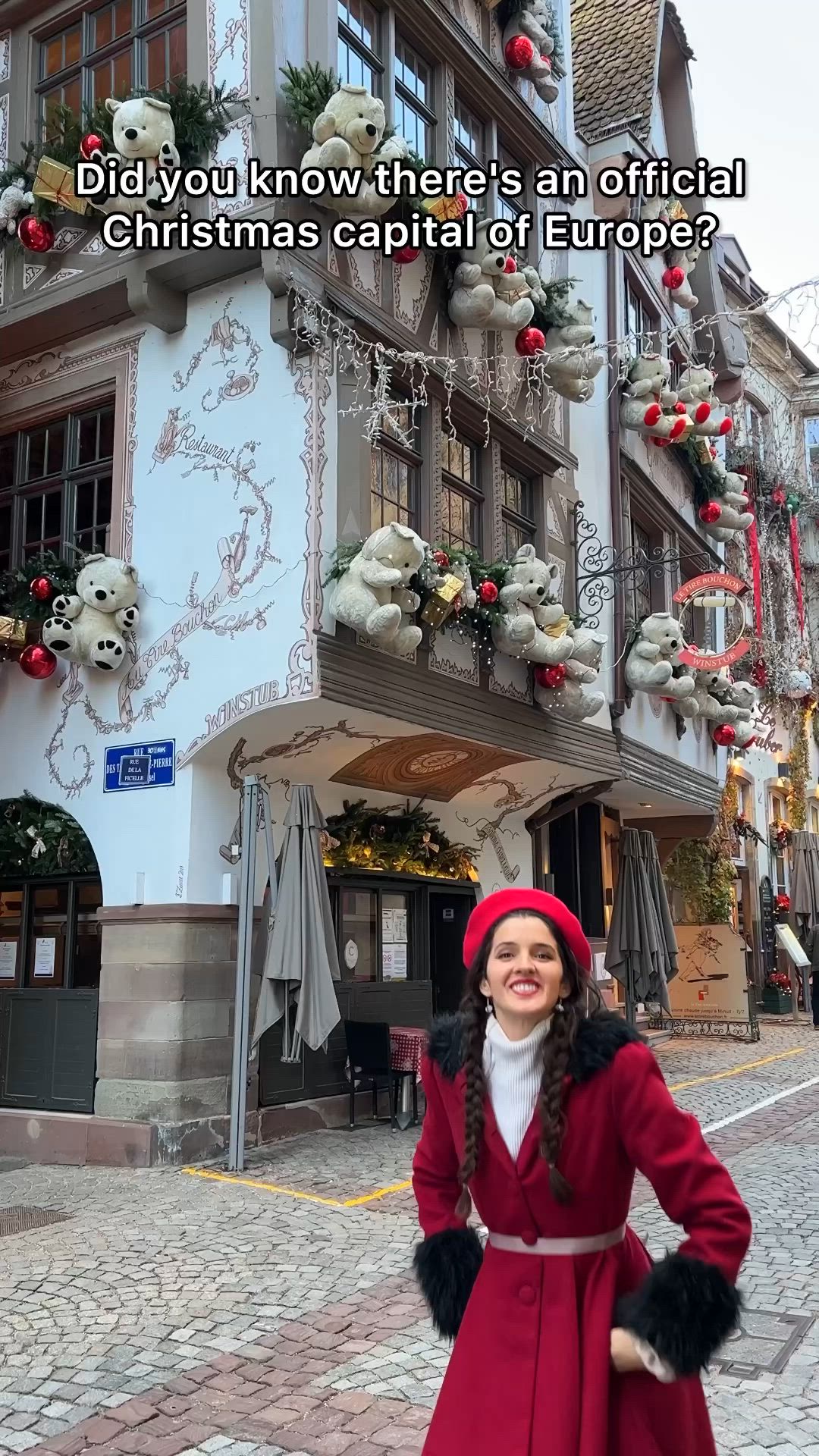 This may contain: a woman standing in front of a building wearing a red coat and fur stoler