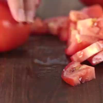 This may contain: sliced up tomatoes on a cutting board being held by someone using a knife to cut them