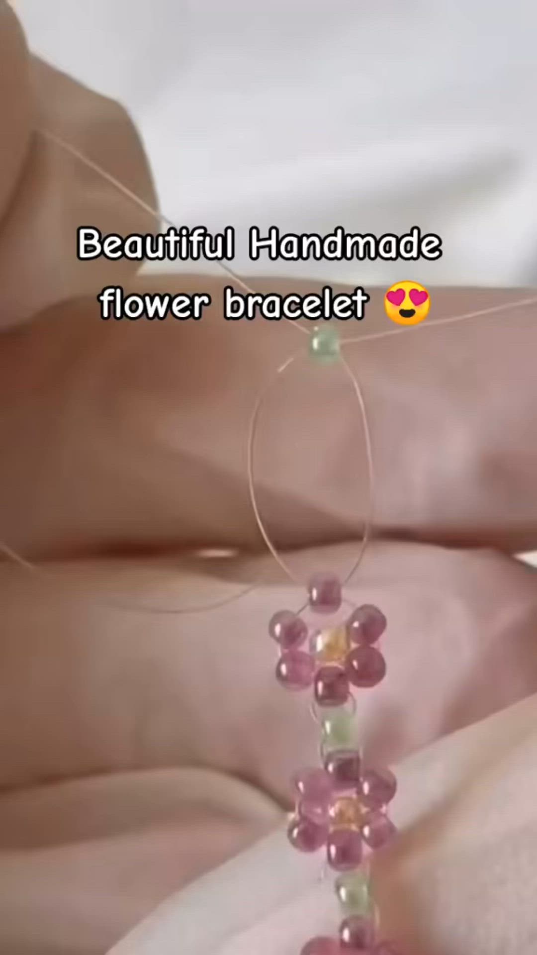 This may contain: someone is making beaded bracelets with pink and green beads on their fingers, while another person's hand holds the string