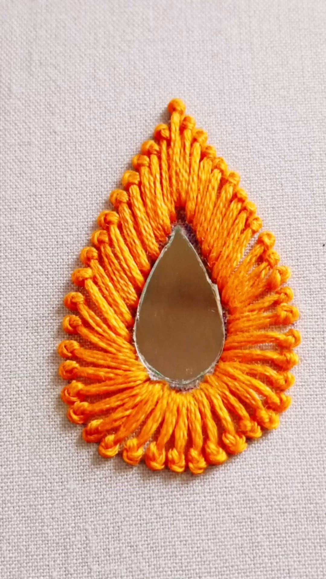 This may contain: an orange and yellow brooch with a tear shaped mirror on the bottom of it