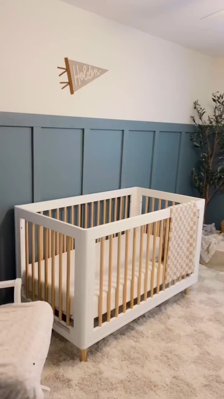 This may contain: a white crib in a room with blue paneling and a plant on the wall