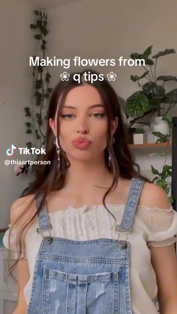 This may contain: a woman wearing overalls making a funny face with her tongue out and the caption'making flowers from q tips '