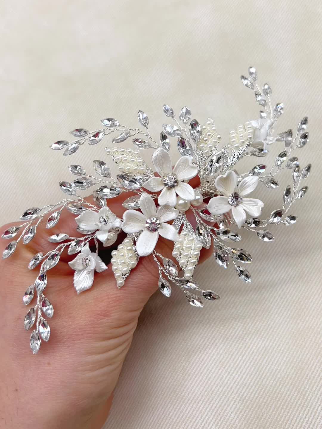 This may contain: a close up of a person's hand holding a white flower and leaf brooch