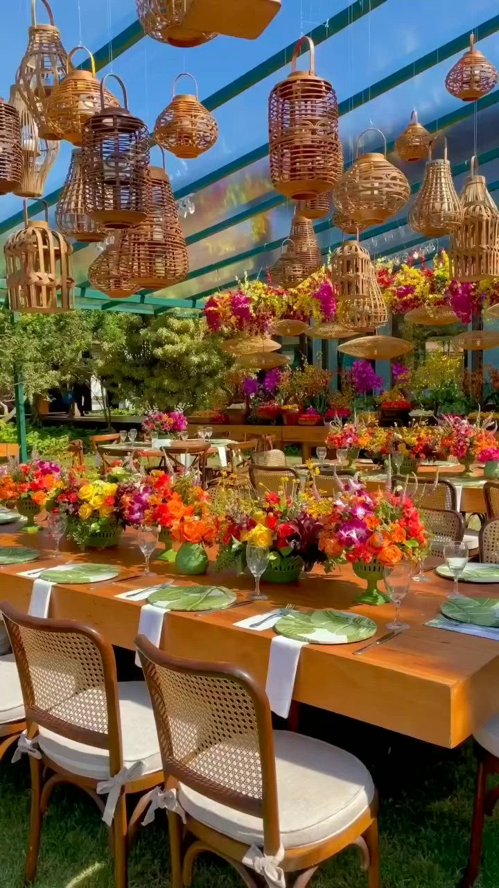 This may contain: an outdoor dining area with tables, chairs and hanging lights filled with colorful flower arrangements