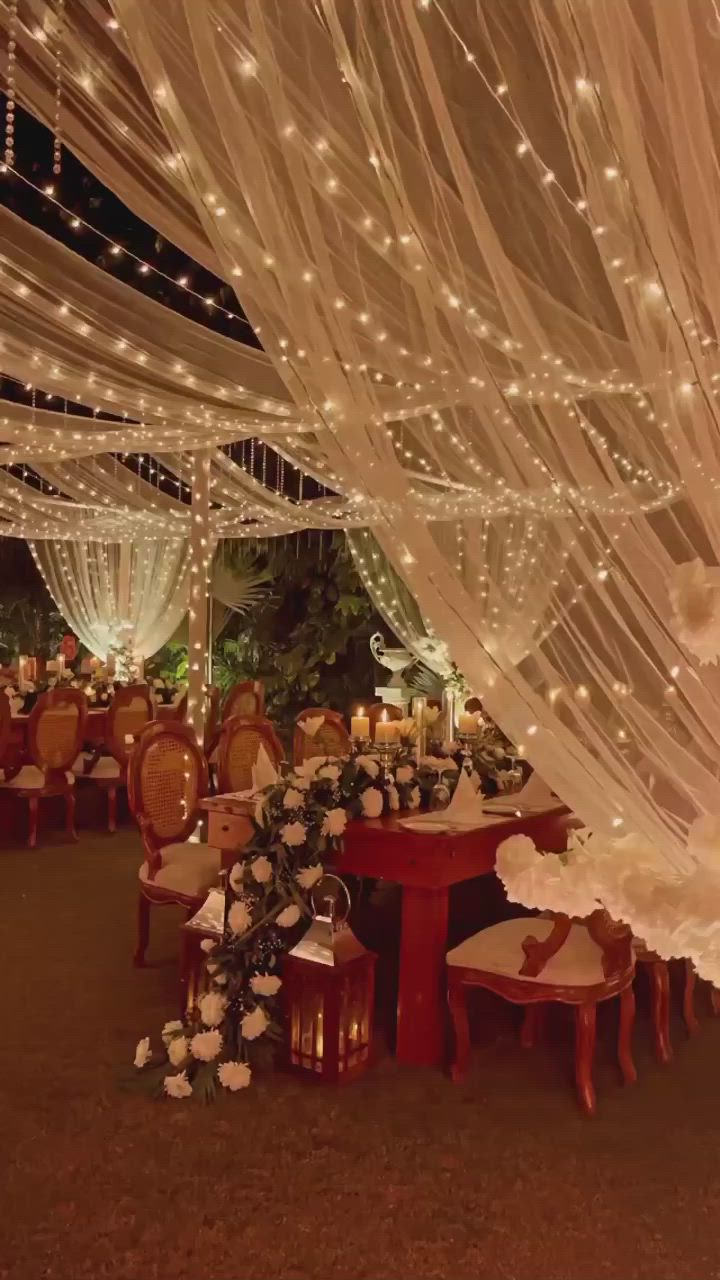 This may contain: an indoor wedding venue with white lights and draping over the top of tables