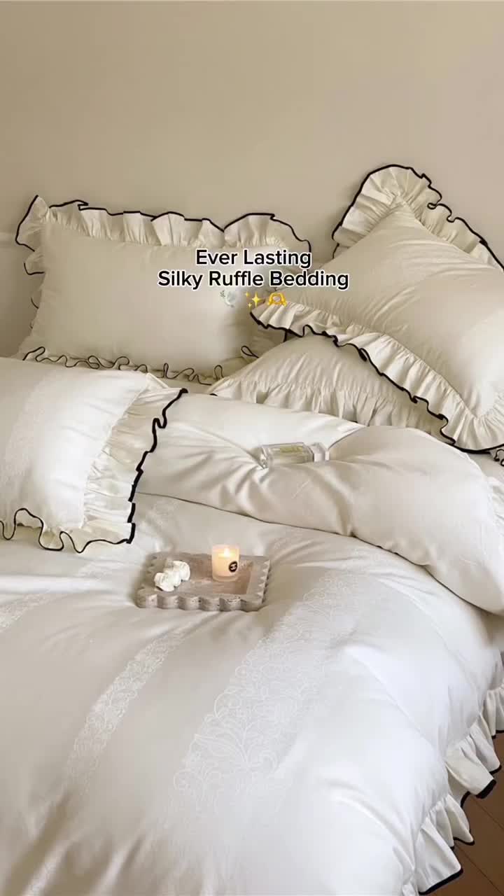 This may contain: a bed with white sheets and ruffles is shown in this image, it has a candle on the pillow