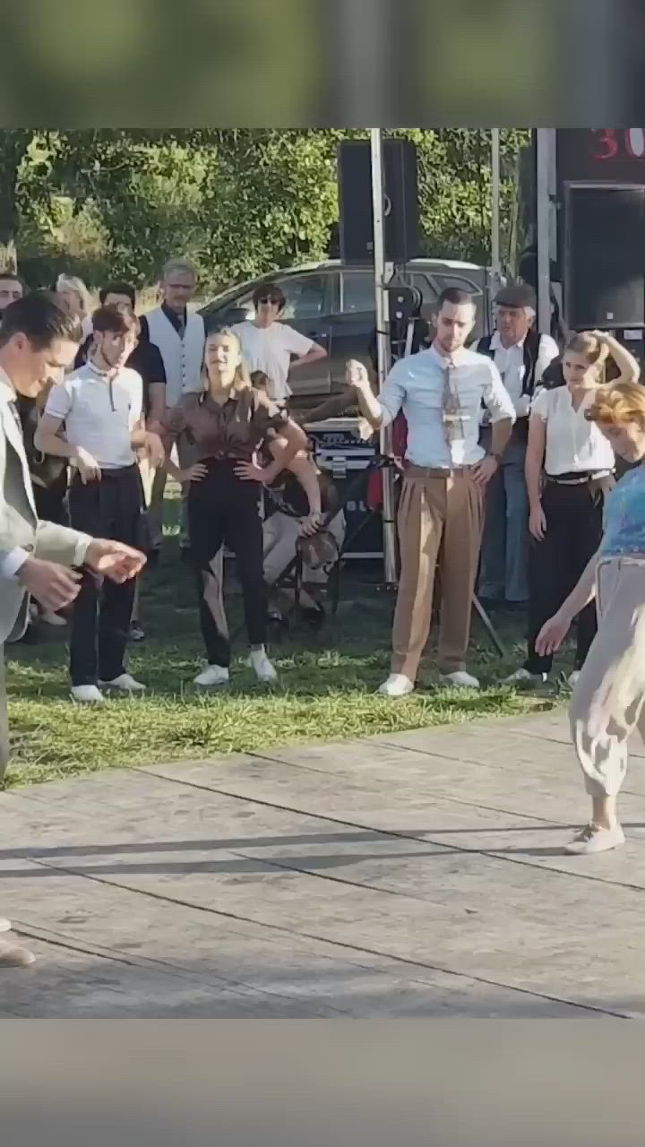 This may contain: two people are dancing on the sidewalk in front of a group of people watching them