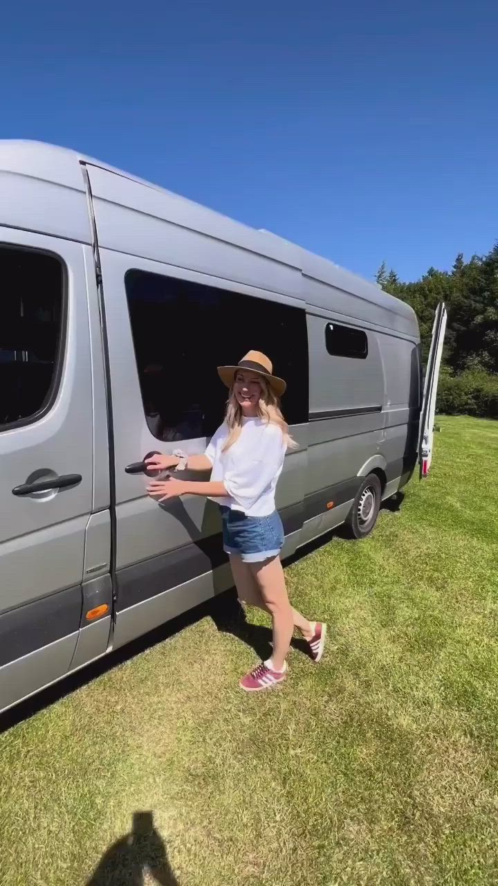 This may contain: a woman standing in front of a van with her hand on the side door window