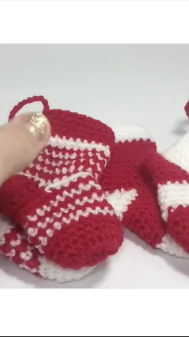 This may contain: a hand is holding a red and white knitted mitt next to a pair of gloves