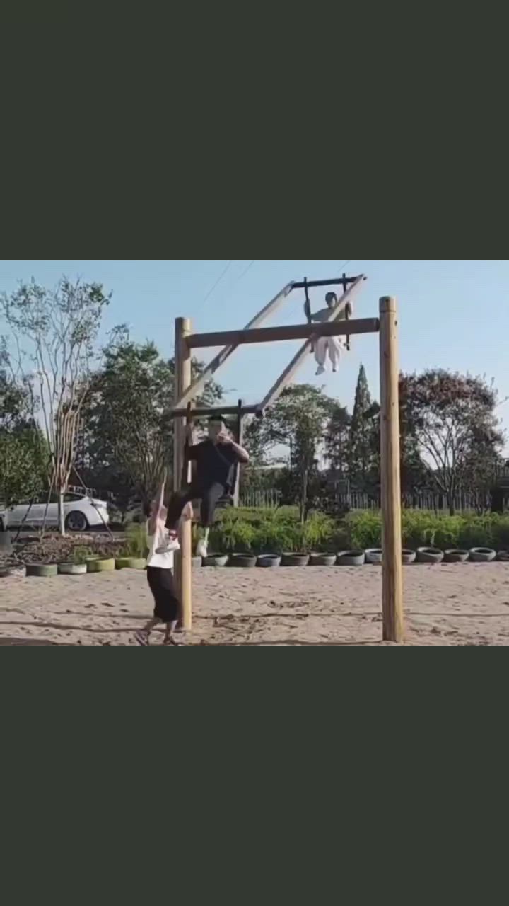 This may contain: two people playing basketball in the sand near a wooden pole and fence with trees behind them