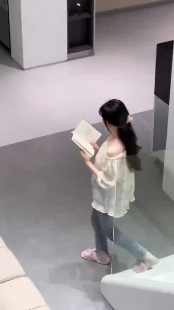 This may contain: a woman standing in front of a mirror holding a book and looking at the floor