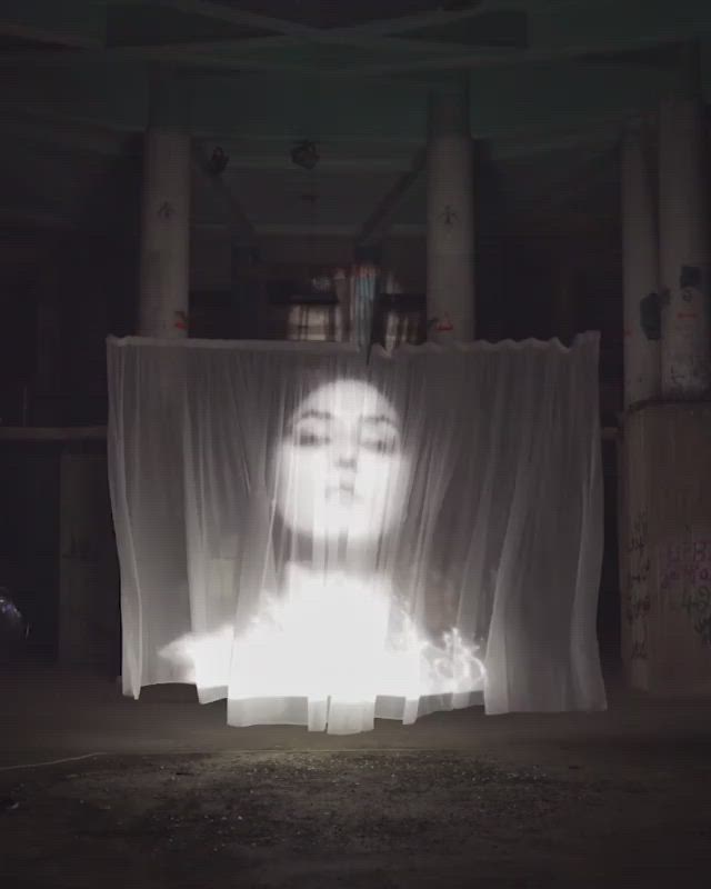 This may contain: a woman's face is projected through curtains in the middle of a dark room