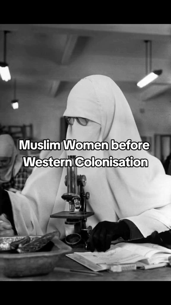 This may contain: a woman wearing a hijab sitting at a table in front of a microscope