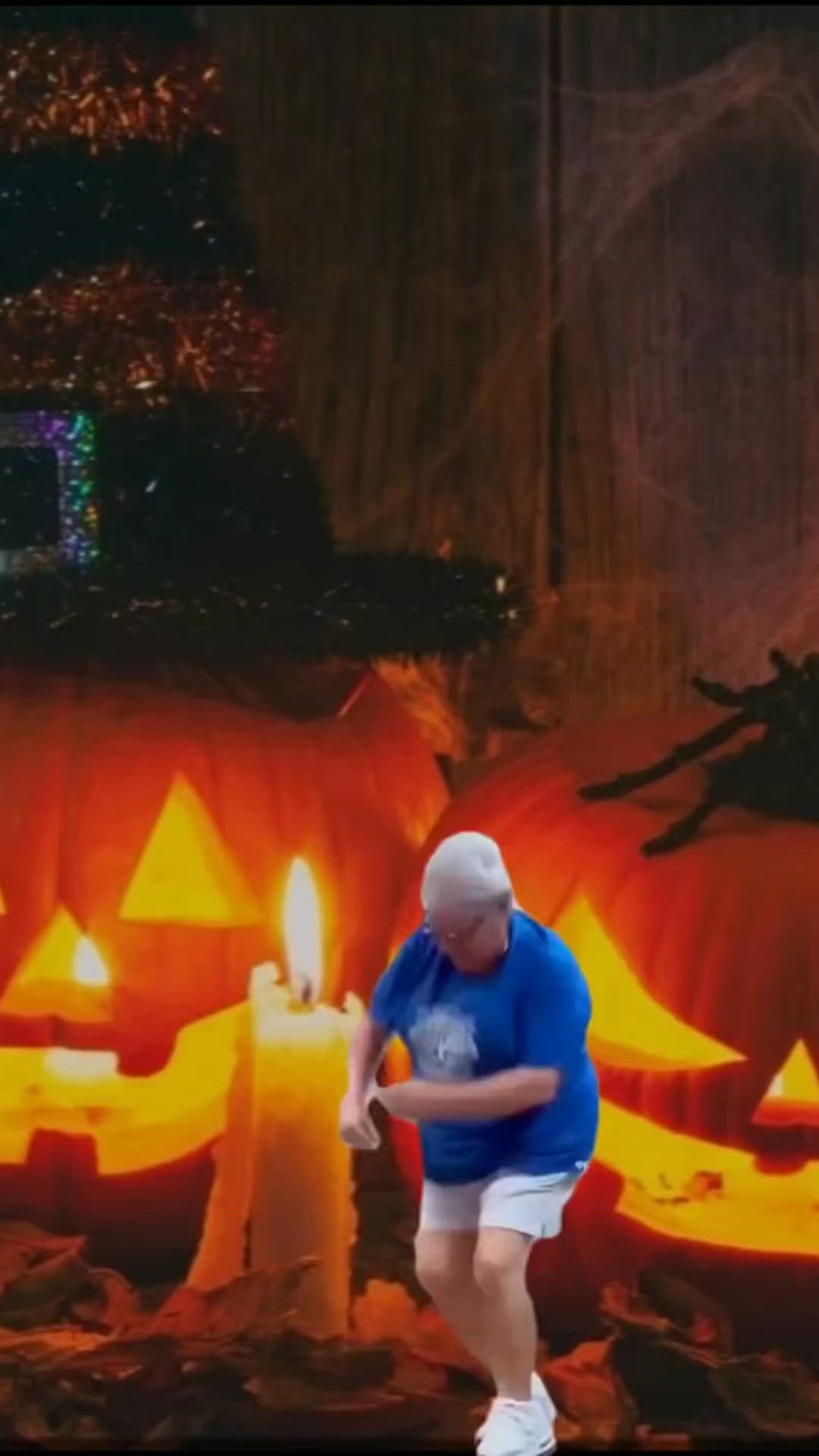 This may contain: a man in blue shirt and white shorts standing next to pumpkins with lit candles