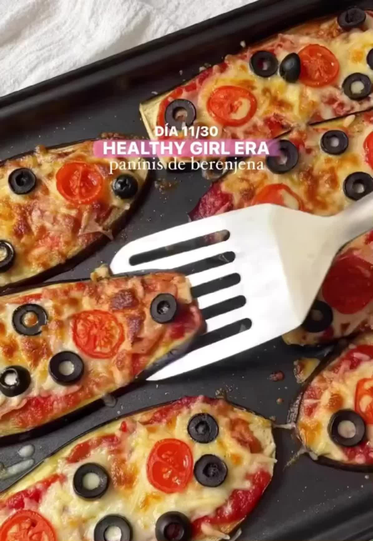 This may contain: pizza with olives, tomatoes and black olives on it is being cut by a spatula