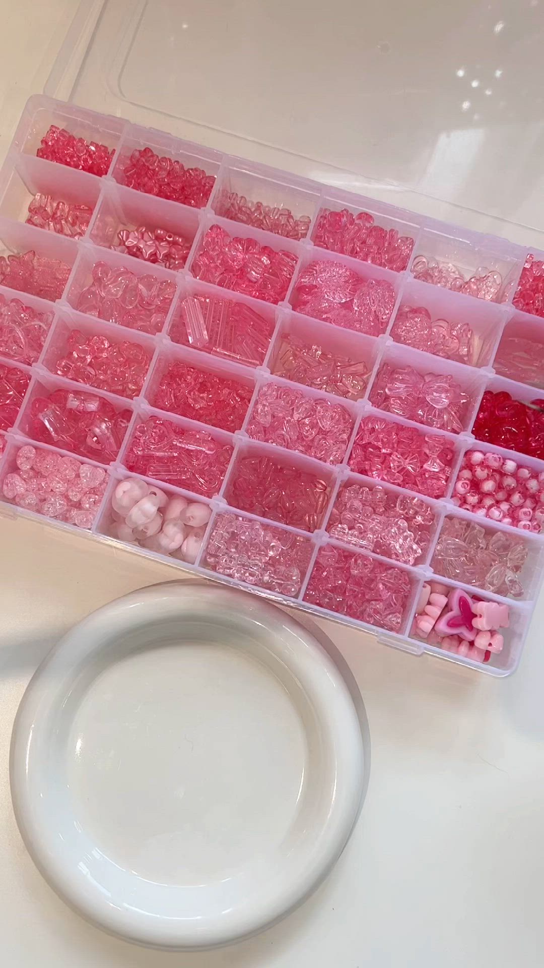 This may contain: a plastic container filled with lots of pink and red beads next to a white plate