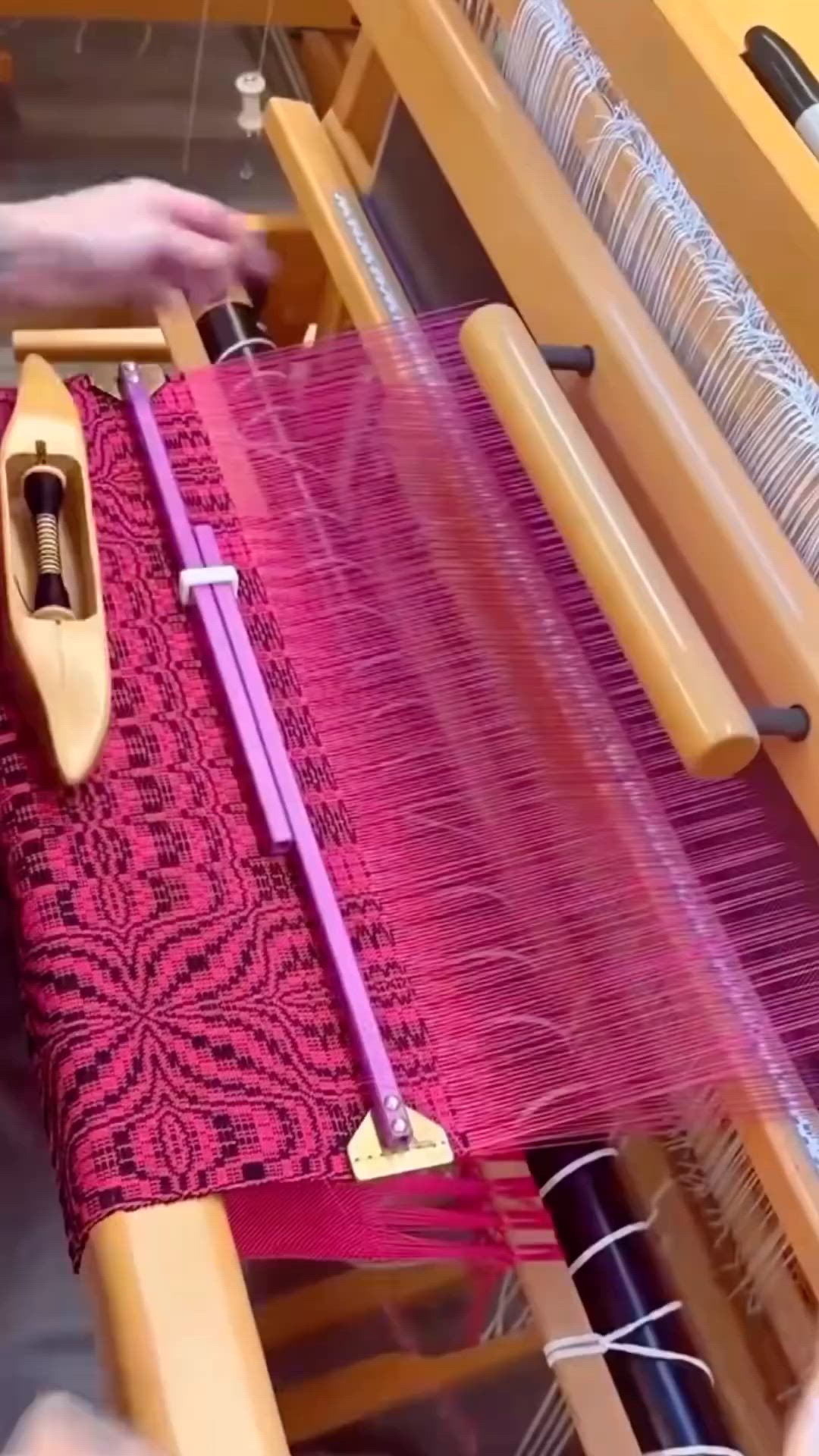 This may contain: a woman is weaving fabric on a loom with a pink and purple color scheme