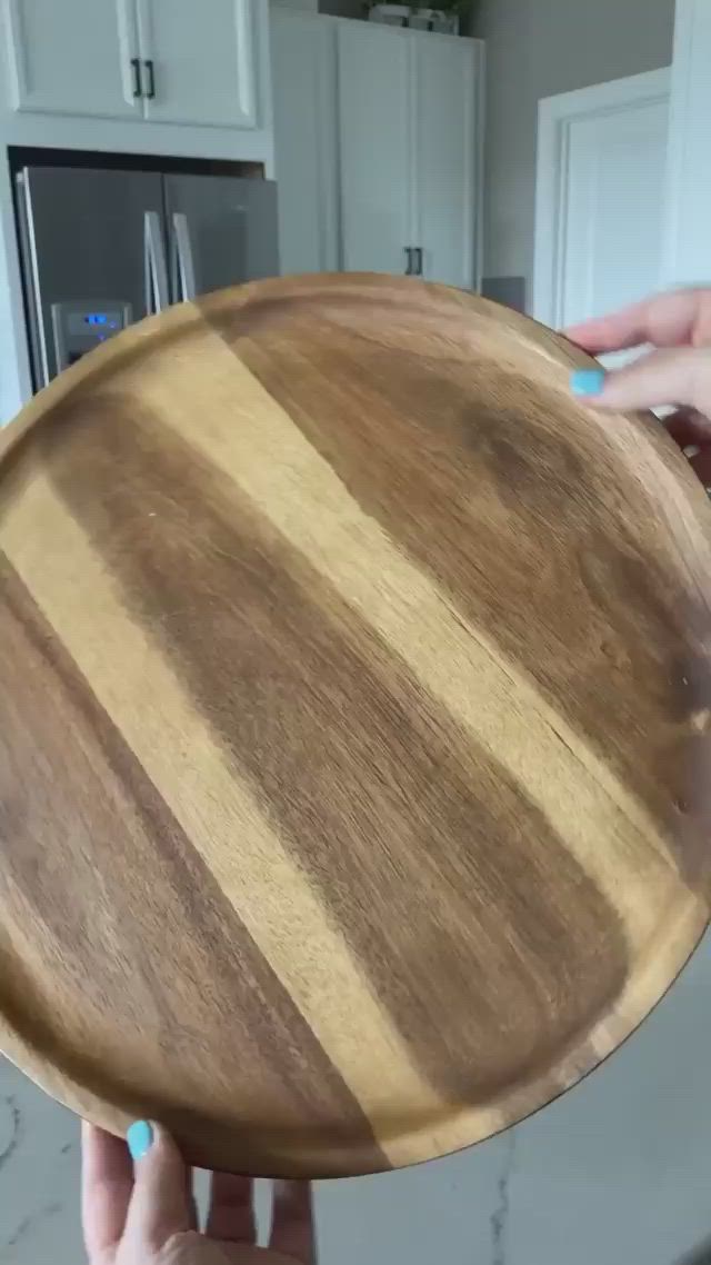 This may contain: a person holding a wooden plate in their hand with white cabinets behind it and blue nail polishing on the edge