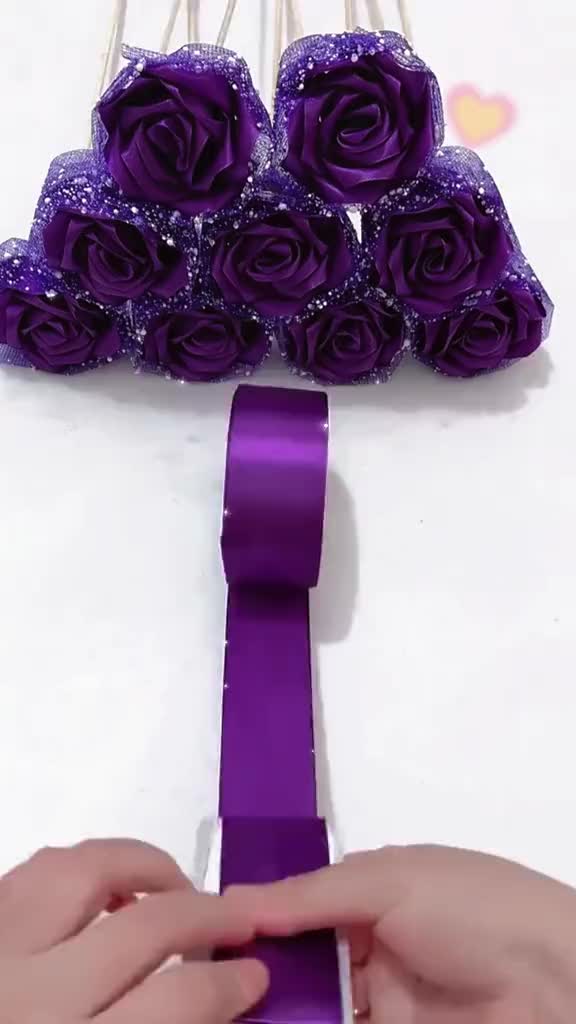 This may contain: someone is making purple flowers out of paper and some pins are attached to the ribbon