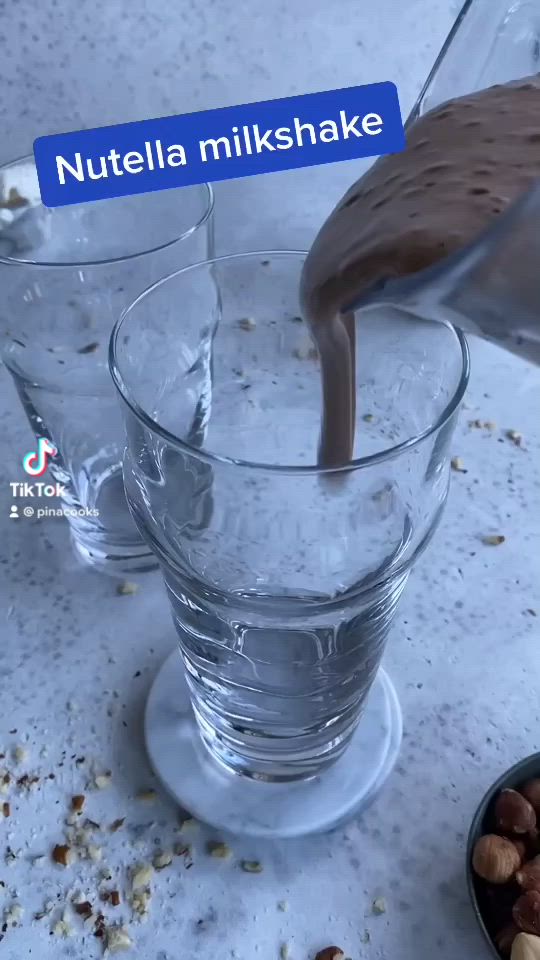 This may contain: nutella milkshake being poured into a glass with nuts in the bowl next to it