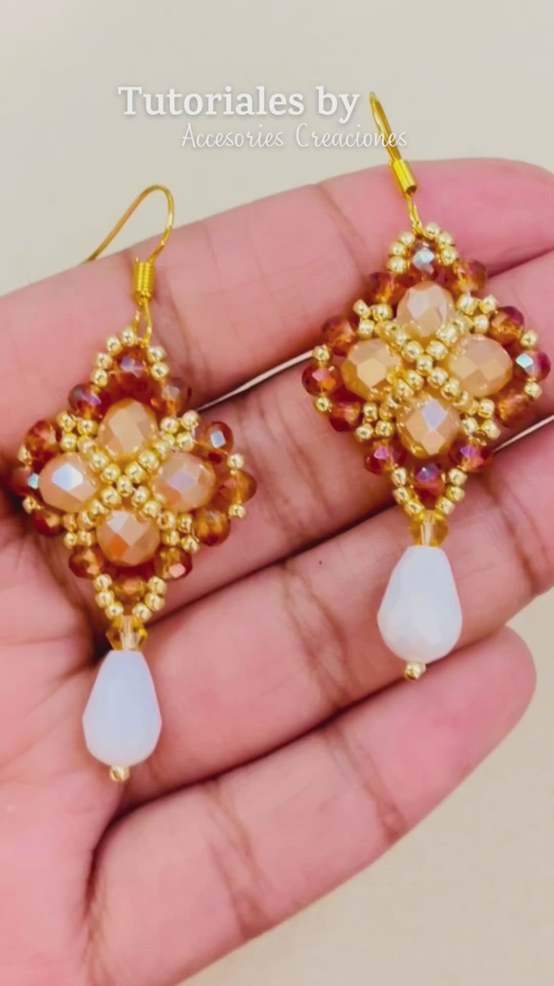 This may contain: a pair of earrings is being held in someone's hand with gold and white beads