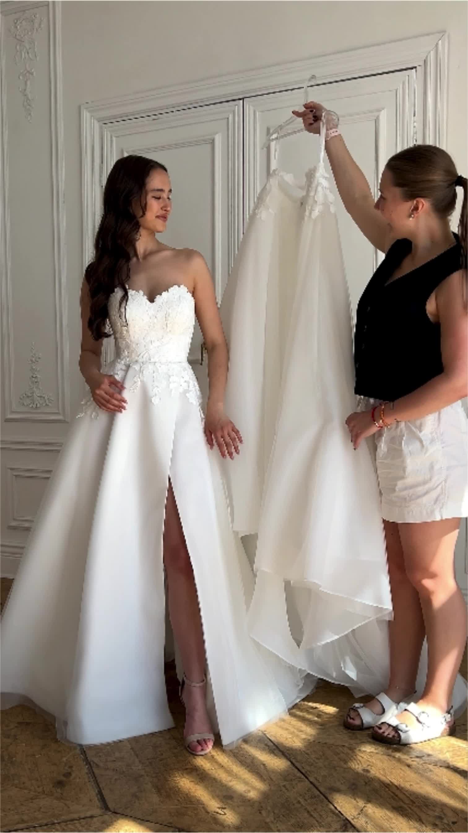 This may contain: two women standing next to each other in front of a white wall holding up dresses