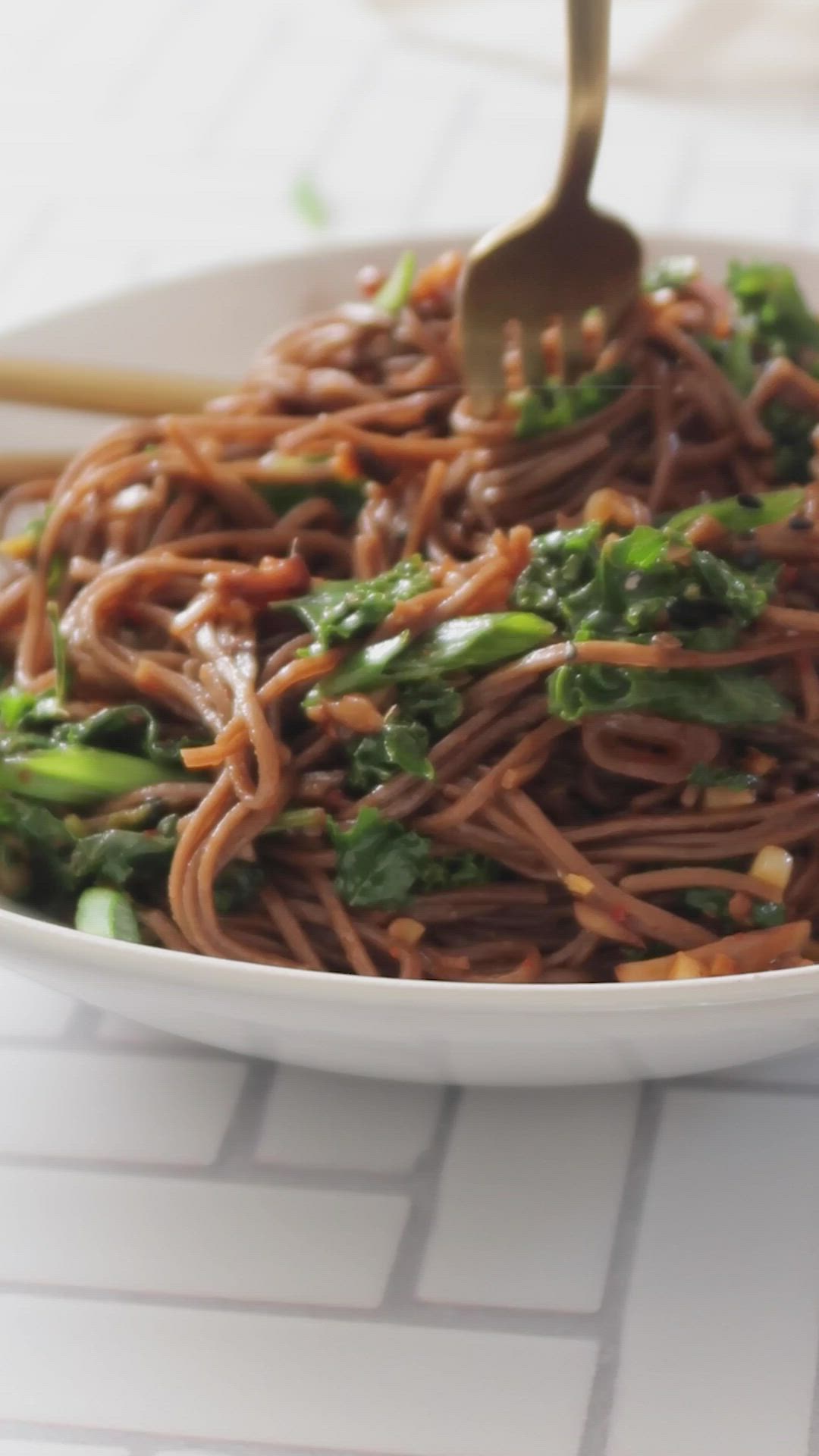 This may contain: a white bowl filled with noodles and broccoli on top of a table next to chopsticks