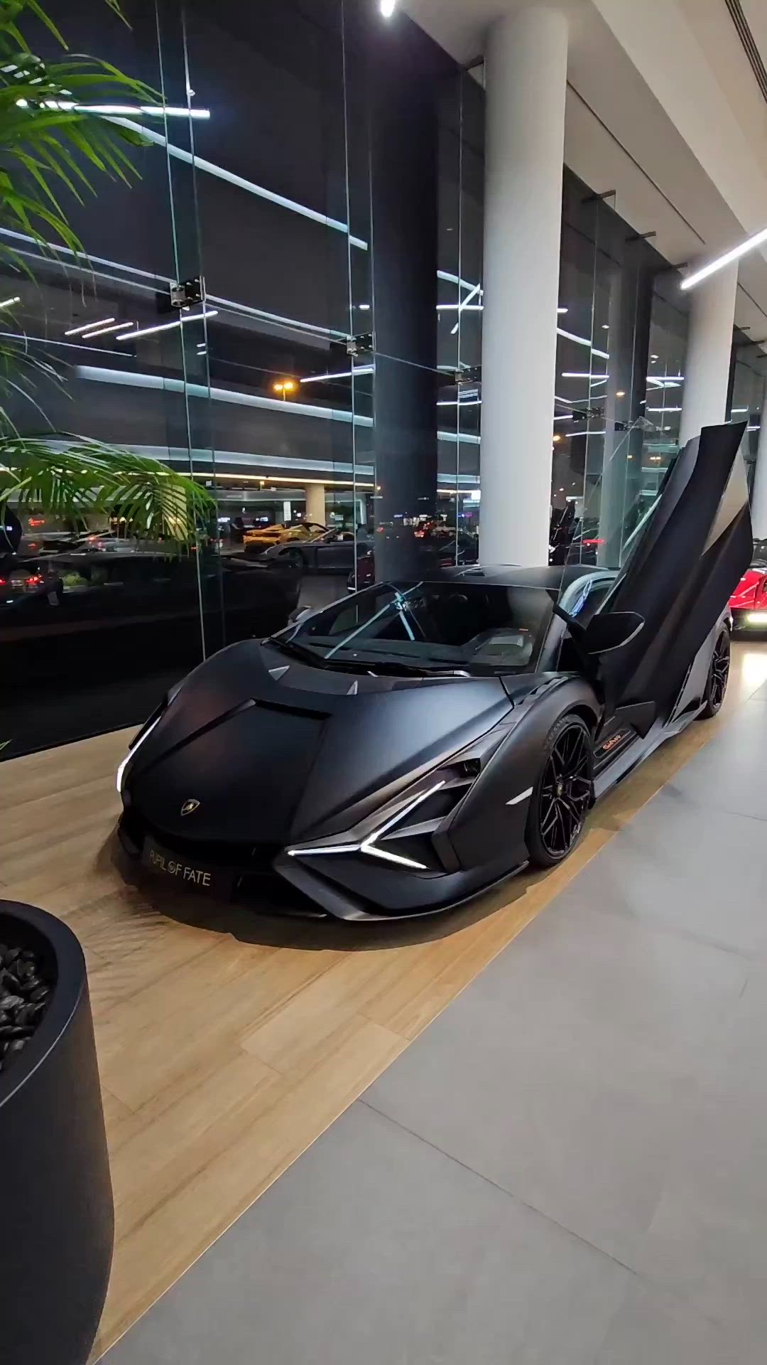 This may contain: a black sports car parked in front of a tall building with glass walls and palm trees