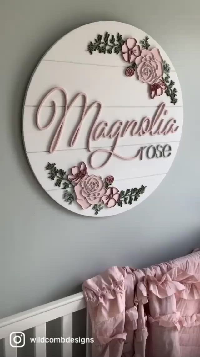 This may contain: a sign that says magnolia rose hanging on the wall above a crib with pink ruffled bedding