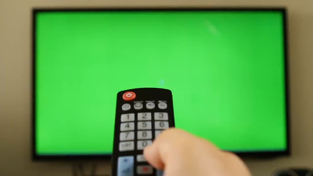 This may contain: a person holding a remote control in front of a television with a green screen on it