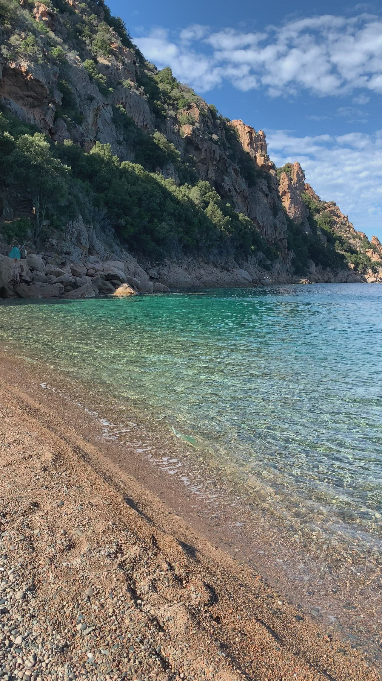 This may contain: a beach with clear blue water next to a rocky cliff and mountain range in the background