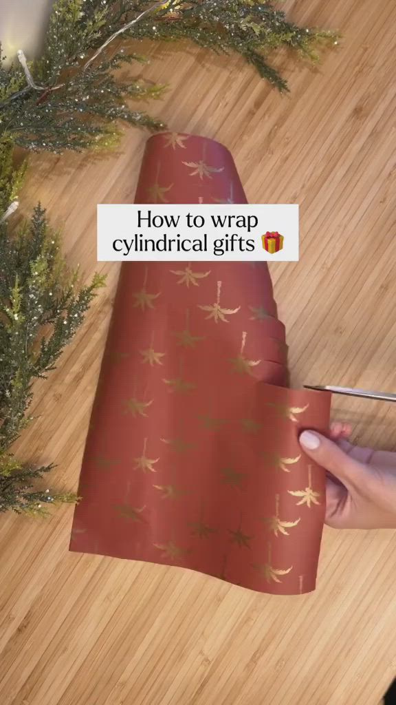 This may contain: someone cutting up wrapping paper on top of a wooden table next to christmas tree branches