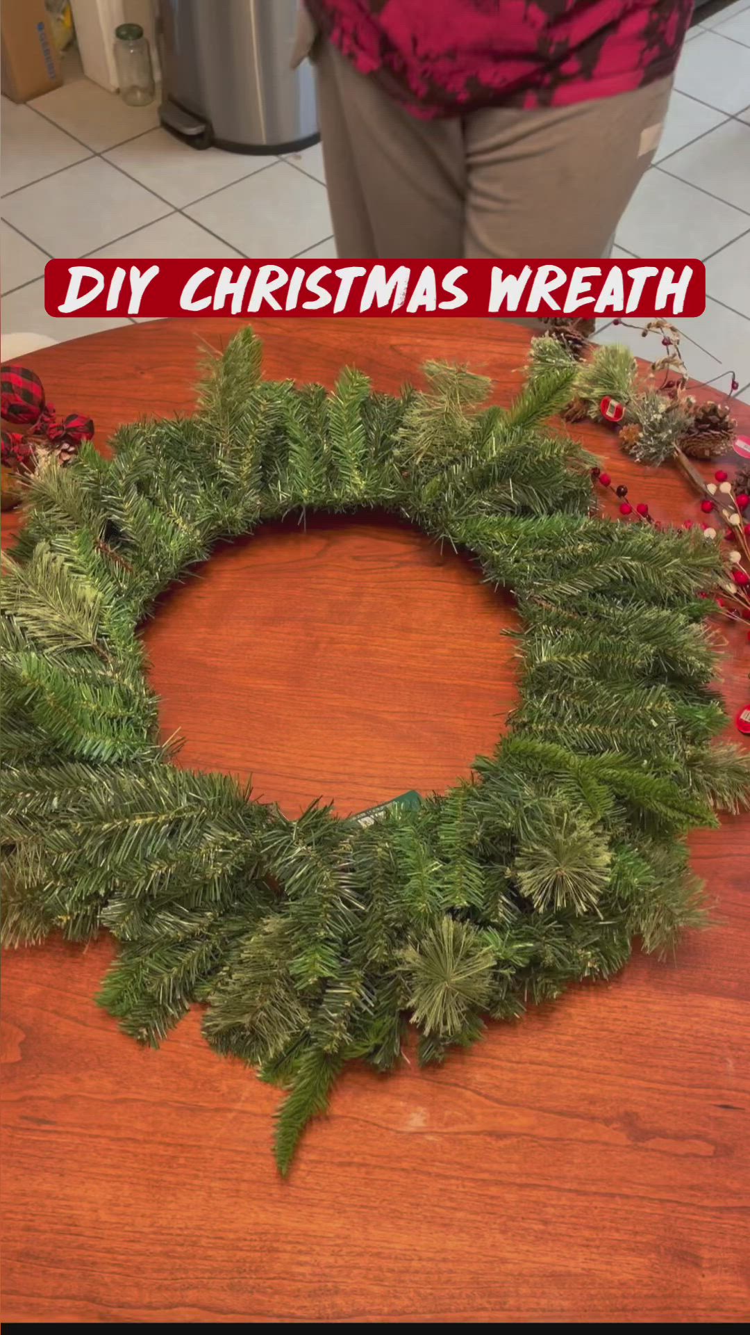 This may contain: a woman is making a christmas wreath out of pine needles and red berries on a wooden table