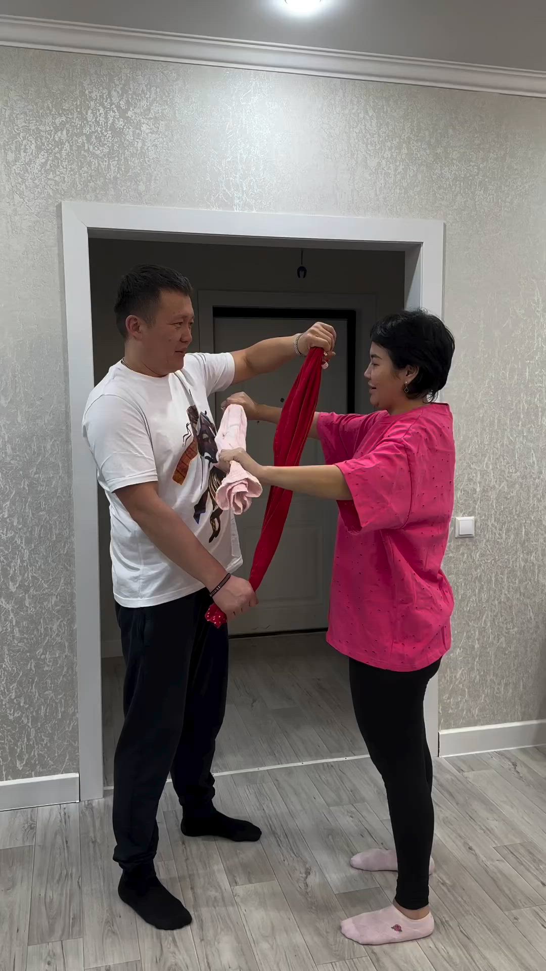 This may contain: a man and woman standing in front of a doorway holding a pink scarf over their heads