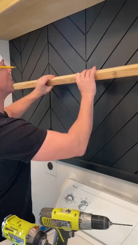 This may contain: a man working on a wall with wood planks in his kitchen area, using a power drill