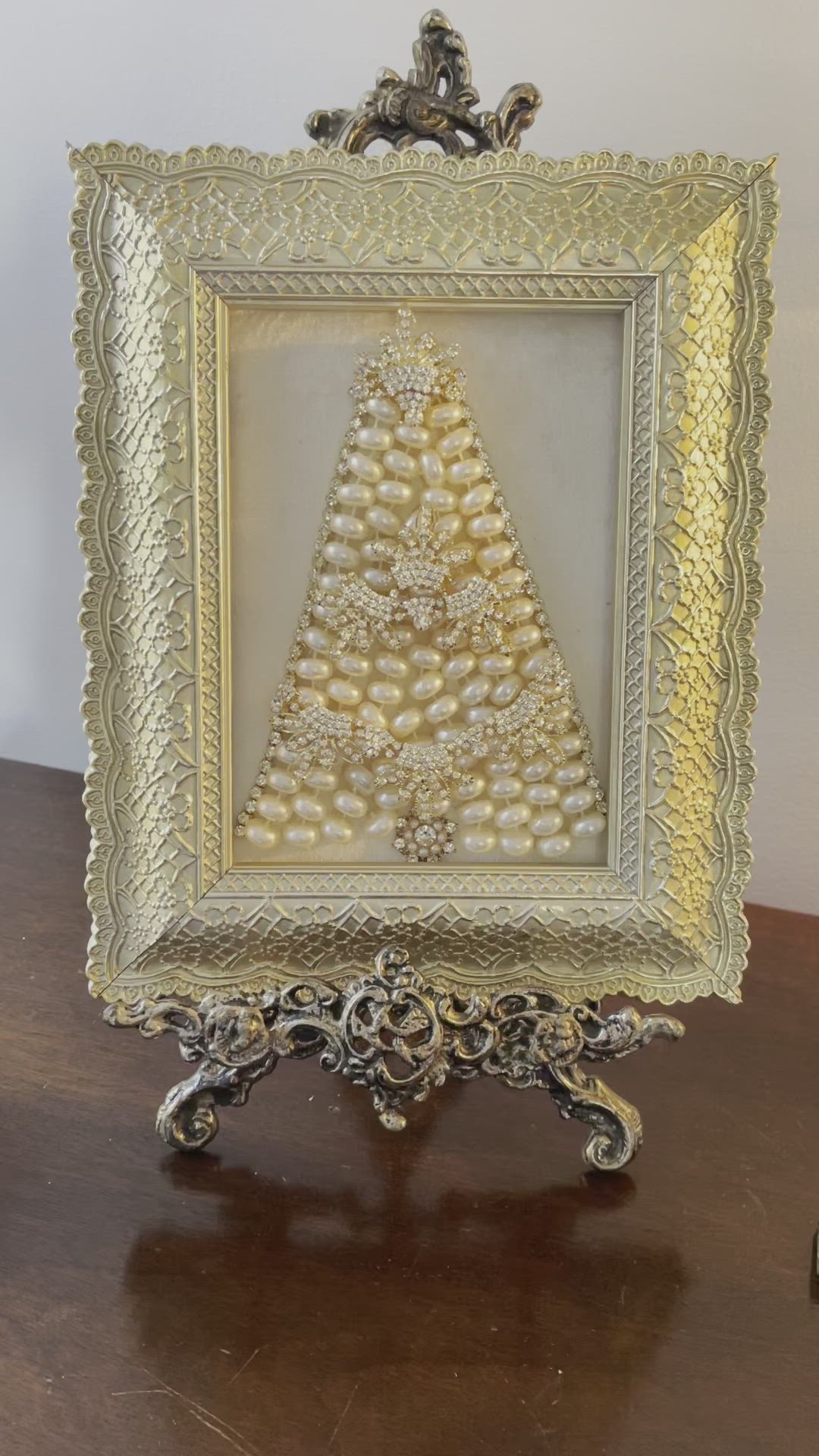 This may contain: an ornate gold frame with a christmas tree in the center on a wooden table next to a white wall