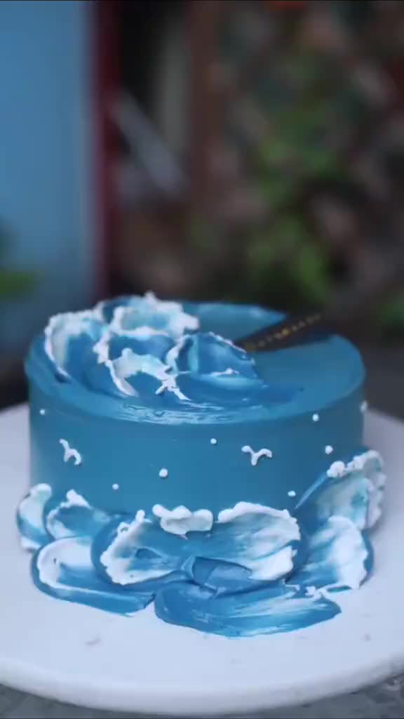 This may contain: a blue cake with white icing on a plate