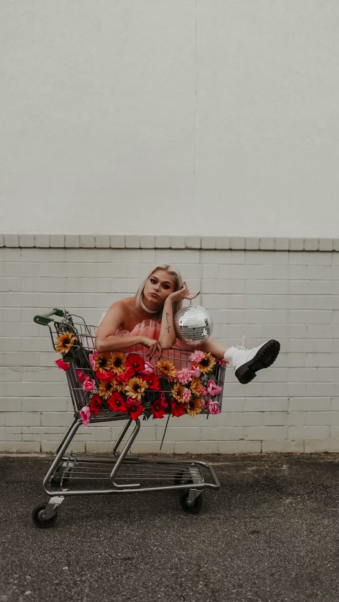 This may contain: a woman laying on top of a shopping cart with sunflowers and flowers in it