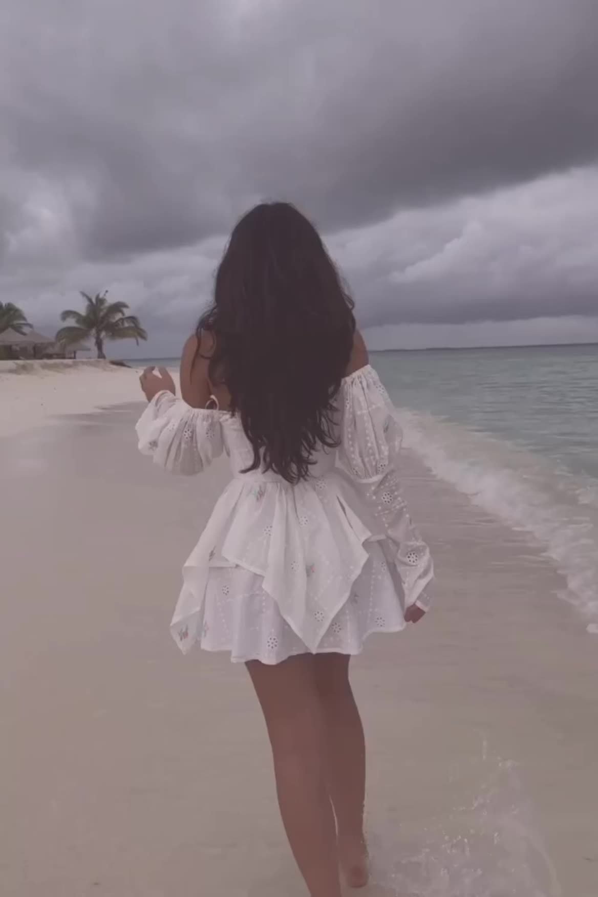 This may contain: a woman is walking on the beach with her back to the camera