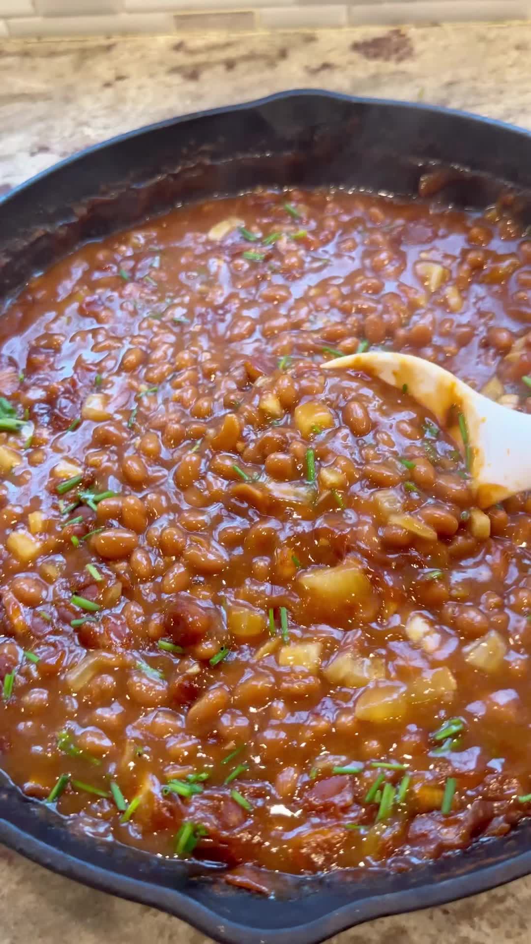 This may contain: a skillet filled with beans and garnish on top of a wooden table