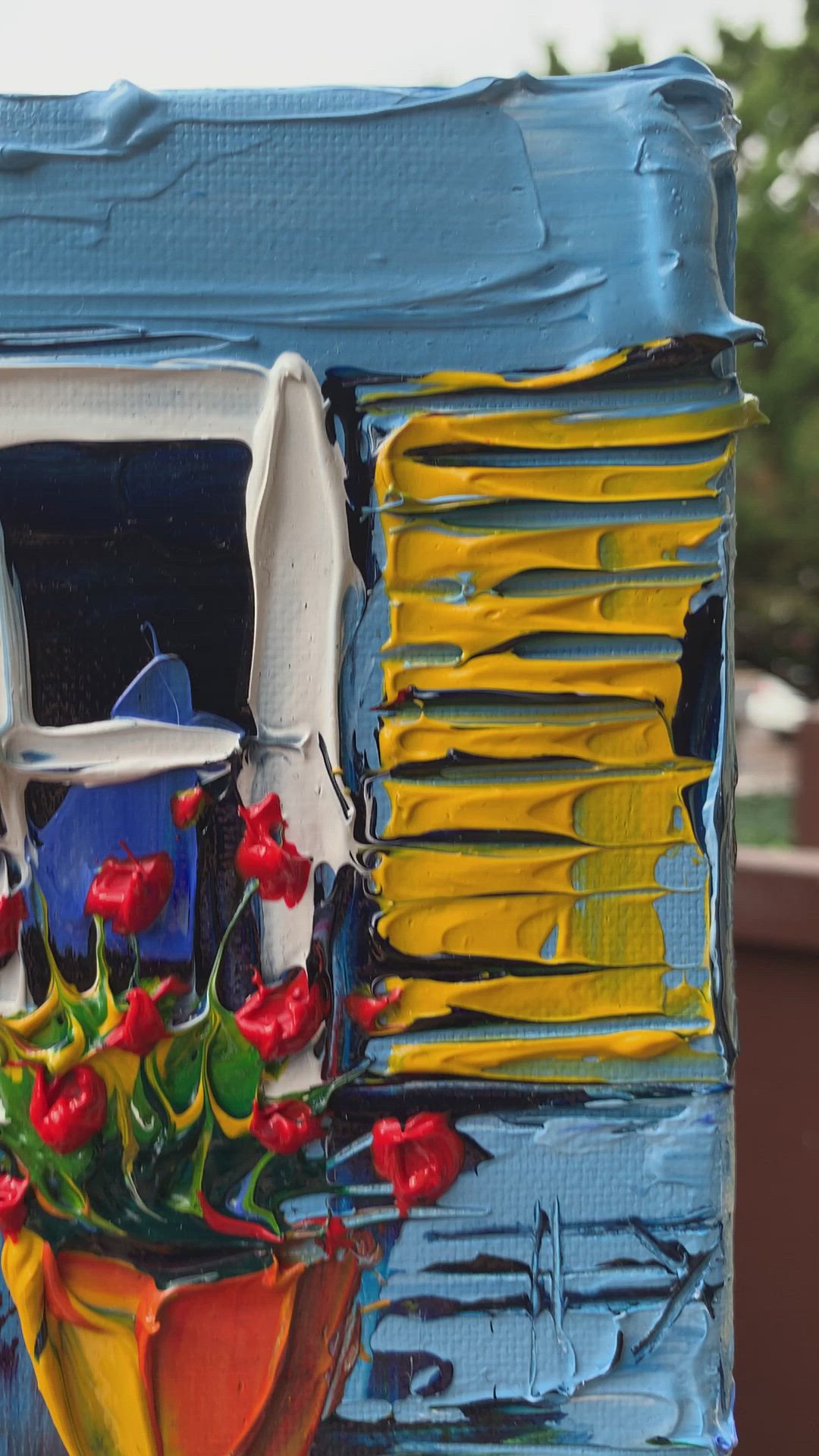 This may contain: a hand holding up a miniature painted window with flowers in the windowsill and potted plants outside