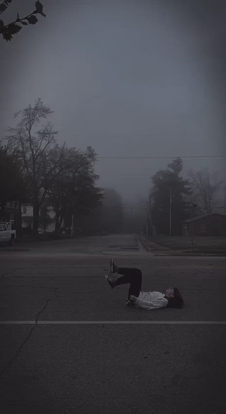 This may contain: a person laying on the ground in an empty parking lot with trees and houses in the background