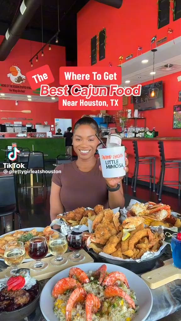 This may contain: a woman sitting at a table full of food and drinks with the caption where to get best cajun food near houston, tx