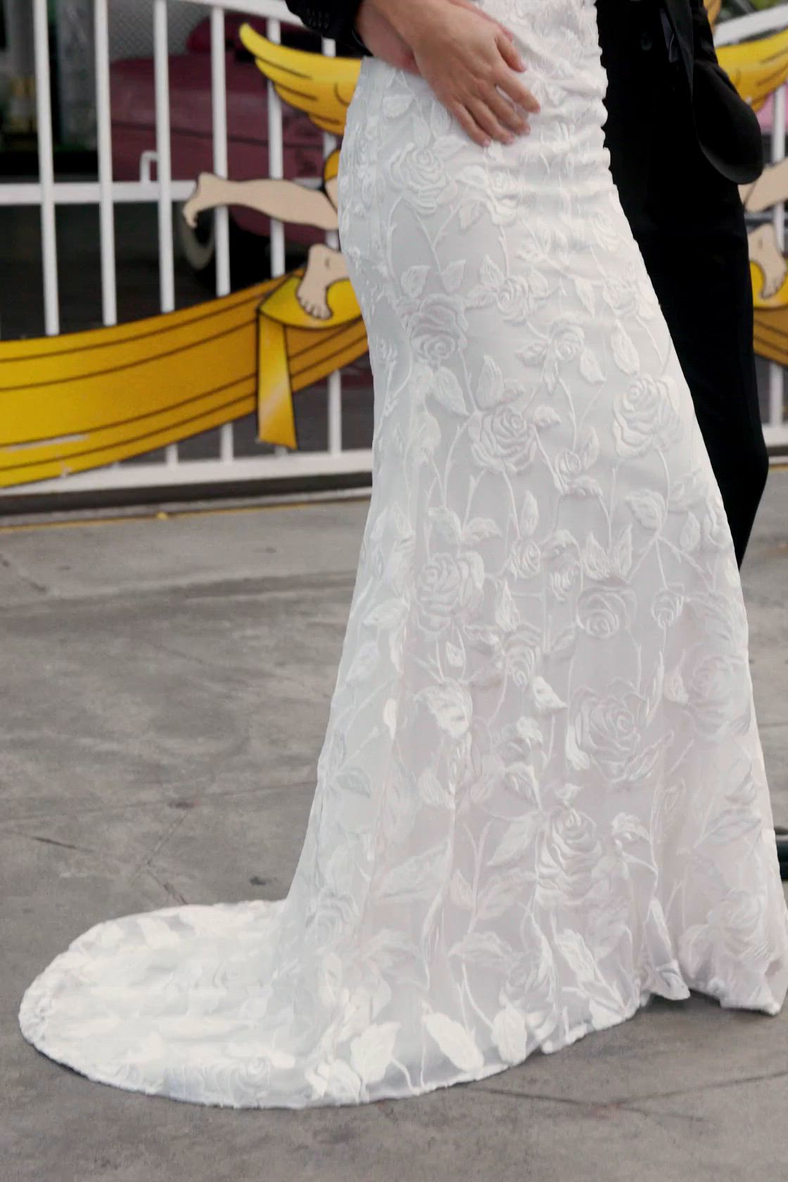 This may contain: a bride and groom standing next to each other in front of a fence with bananas on it