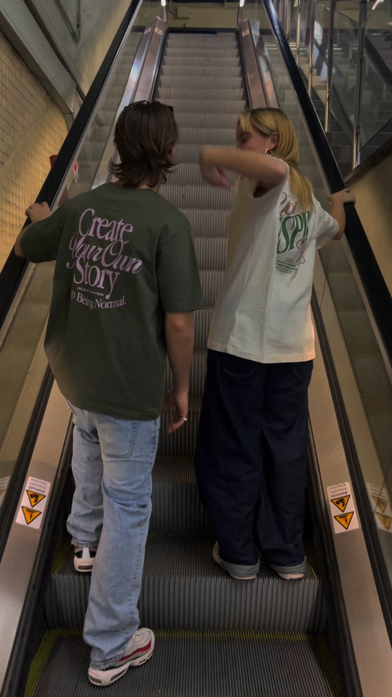 This may contain: two people standing on an escalator pointing at something in the distance with their backs to each other