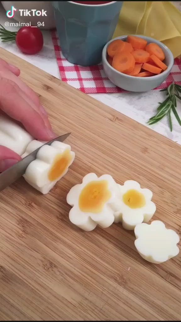 This may contain: someone cutting up boiled eggs with a knife on a cutting board next to carrots